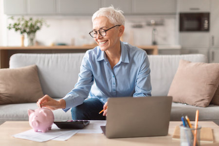 Happy european mature woman holding putting money in piggybank indoorの写真素材