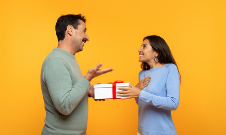 European old man joyfully presents gift to surprised woman, both engagedの写真素材