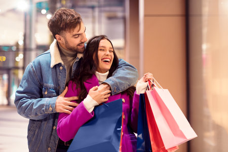 Cheerful buyers couple outside of store hugging with shopping bagsの写真素材