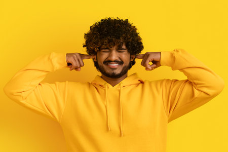 Young dissatisfied annoyed indian man closed eyes cover earsの写真素材