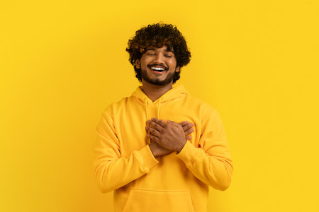 Excited young indian man holding hands on chest over heartの写真素材