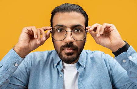 Serious man adjusting stylish round glasses, wearing a blue denim shirt