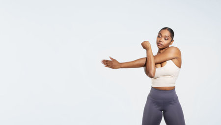 African american fitness lady exercising stretching arms before workout, studioの写真素材