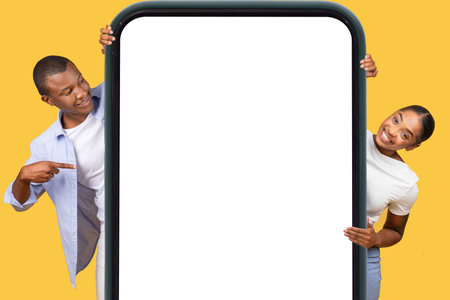 African american couple with big smartphone frame, pointing, yellow backgroundの写真素材