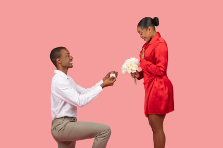 Black man proposing with ring, woman with flowers, surprised and happyの写真素材