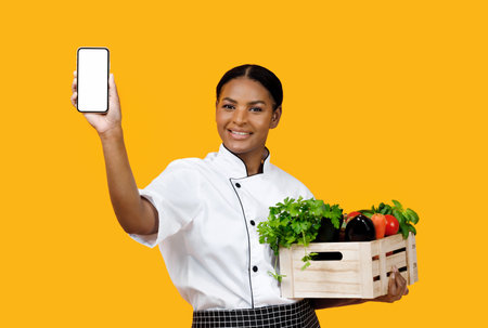 Grocery Market App. Cheerful Black Chef Woman Showing Smartphone With Empty Screenの写真素材