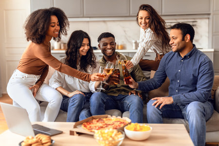 Diverse group of students clinking with beer on sofa indoorsの写真素材