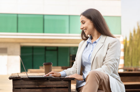 Cheerful young professional woman working on her laptop at an outdoor settingの写真素材