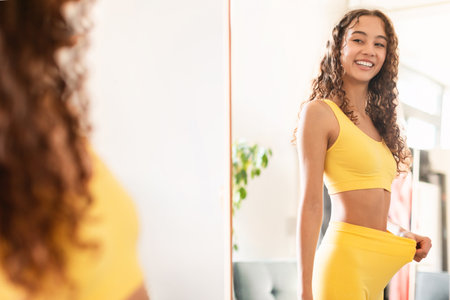 teen girl looking in mirror showing result of slimming indoorの写真素材