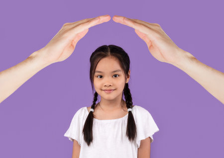 Happy school aged asian girl under hands roofの写真素材