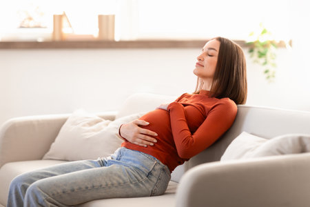 Pregnant european lady rests peacefully on living room couch indoorの写真素材