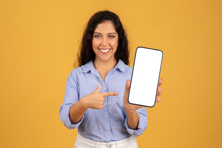 Confident young woman with curly hair presents a smartphone with a blank screenの写真素材