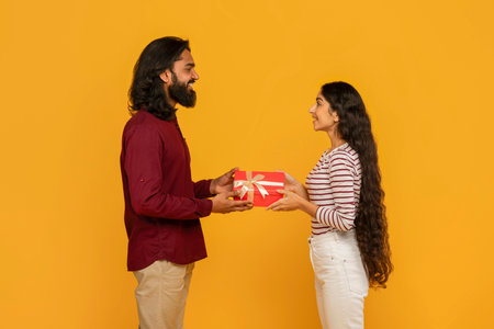 Cute young eastern couple exchanging gifts on yellow backgroundの写真素材