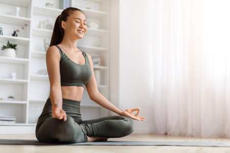 Beautiful young asian woman smiling gently while practicing yoga at homeの写真素材