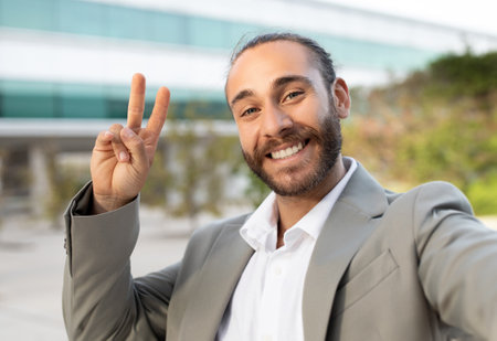 Friendly young businessman in suit making peace sign while taking selfie outdoorsの写真素材