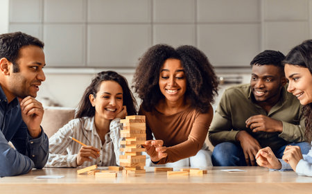 Young diverse friends engaged in board game building tower indoorsの写真素材