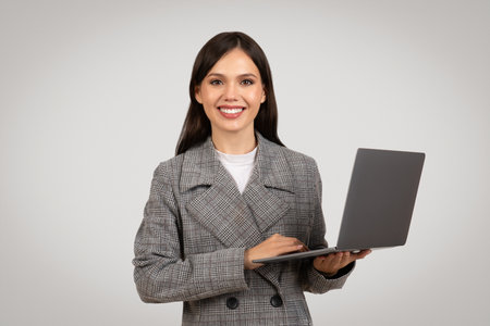 Smiling businesswoman presenting laptop in checkered suit, tech savvyの写真素材
