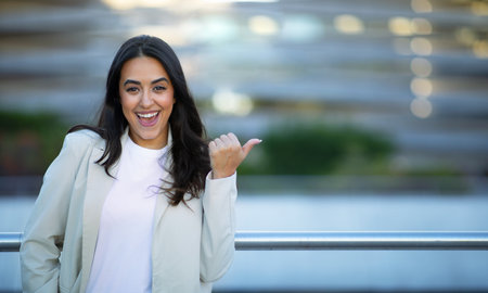 Cheerful Arabic Businesswoman Pointing Thumb Aside At Copy Space Outdoorsの写真素材