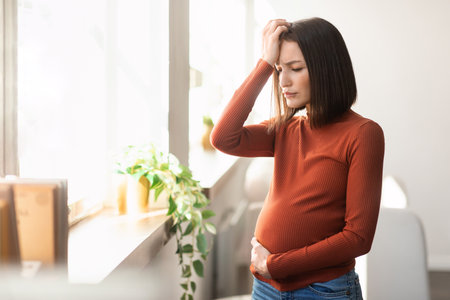Young pregnant lady suffering from migraine and flu symptoms indoorsの写真素材
