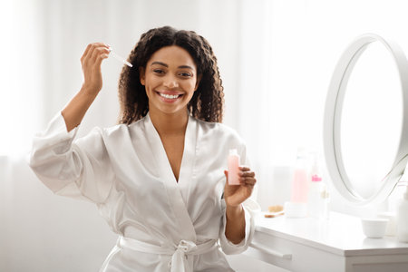 Beautiful Black Female Applying Moisturising Serum On Face At Homeの写真素材