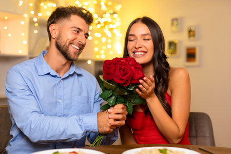 Smiling man presenting roses to delighted woman, joyful dinner momentの写真素材