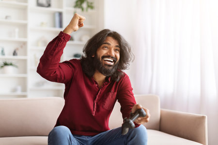 Excited emotional indian man gamer sitting on couch at home
