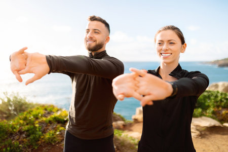 Sporty couple stretching arms outdoors, sunny coastal backgroundの写真素材