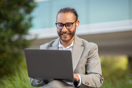 Focused young man in eyeglasses working on laptop outsideの写真素材