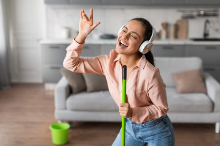 Delighted young woman singing with mop while doing houseworkの写真素材