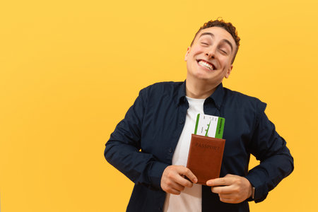 Overjoyed young guy tourist showing passport with flight ticketsの写真素材