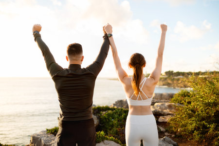 Triumphant couple with raised arms facing the oceanの写真素材