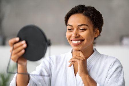 Self-Care Concept. Beautiful Black Woman Holding Handheld Mirror And Touching Faceの写真素材