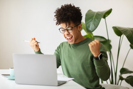 Emotional african american guy celebrating success, working at cafeの写真素材