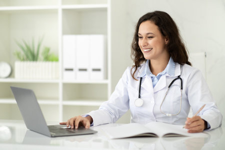 Young woman doctor using laptop at clinic, telemedicine concept