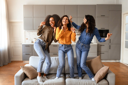 Three multiracial young ladies laughing and dancing in living room