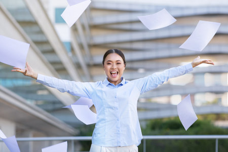 Happy young asian businesswoman throwing business papers in air outdoorsの写真素材