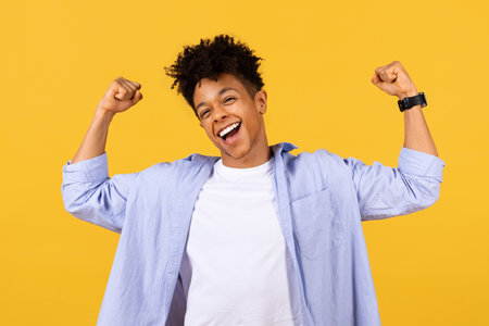 Euphoric black male student celebrating success on yellow backdropの写真素材
