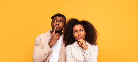 Pensive black couple in casual wear on yellow backdropの写真素材