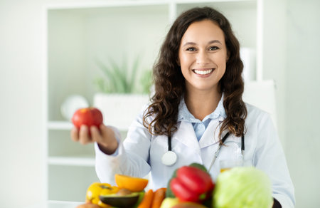 Young european woman dietitian holding apple, sitting at desk at clinicの写真素材