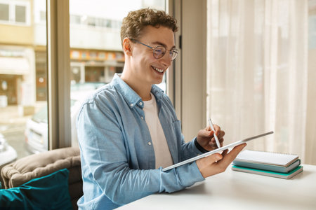 Cheerful millennial european guy designer in glasses using pen and digital tablet for paintの写真素材