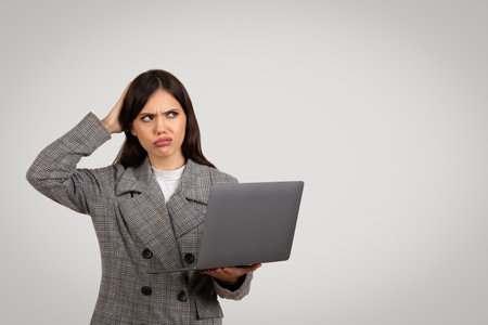 Puzzled woman with laptop, scratching head, copy space