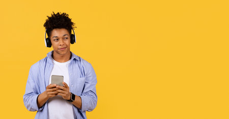 Teen with headphones browsing phone on yellow background, copy space