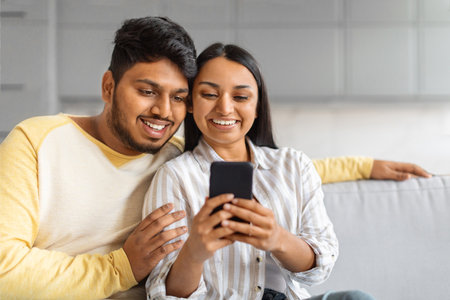 Portrait Of Happy Indian Couple Resting With Smartphone On Couchの写真素材