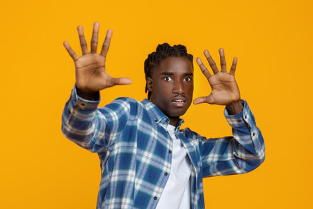 Scared young black man in plaid shirt raising hands and saying stop