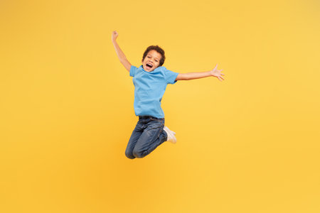 Ecstatic black boy jumping with joy on yellow backgroundの写真素材