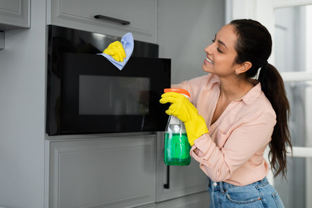 Woman cheerfully cleaning microwave with spray and clothの写真素材