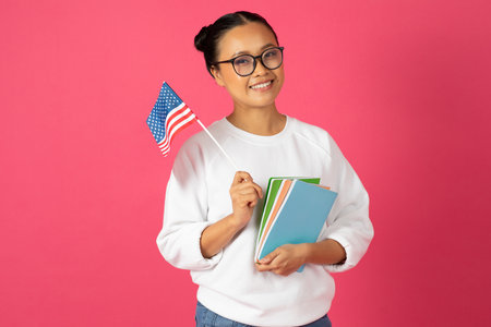 Smiling asian student woman proudly holding American flag and colorful notebooksの写真素材
