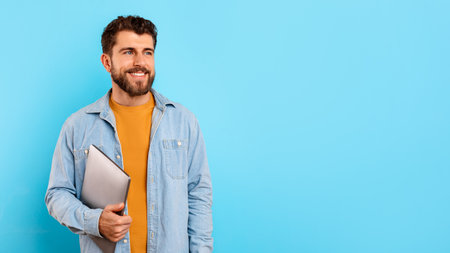 Happy young man holding his laptop computer on blue backgroundの写真素材