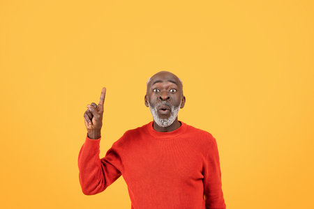 Surprised and excited elderly man in a red sweater pointing upwardsの写真素材