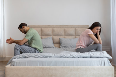 Young couple having relationship difficulties, sitting on opposite sides of bed, ignoring each other at homeの写真素材